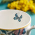 1 | Blue butterfly inside the Kruger Mug designed by Emma J Shipley, crafted in fine bone china by skilled artisans in Stoke on Trent UK, hand decorated with an exquisitely detailed and colourful artwork with giraffes and detailed foliage in yellow, blues and greens - part of the Fine China Dining collection