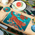 Teal | Medium | 1 | A lifestyle image of the Teal Medium Placemat in the snow leopard design with a rust red leopard surrounded by bright Teal greens and deep blue tones, designed by Emma J Shipley