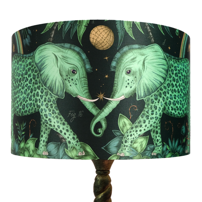 The Large Teal Zambezi Silk Lampshade features two enchanting Zambezi elephants on the front intertwining trunks, with vibrant greens and golds on a deep Navy background